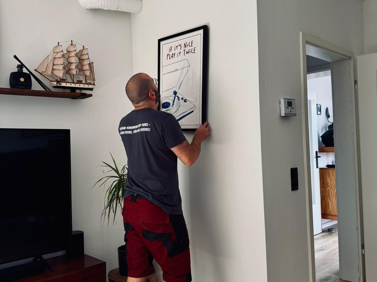 Cem hängt in einem Wohnzimmer ein gerahmtes Bild gerade an die Wand.