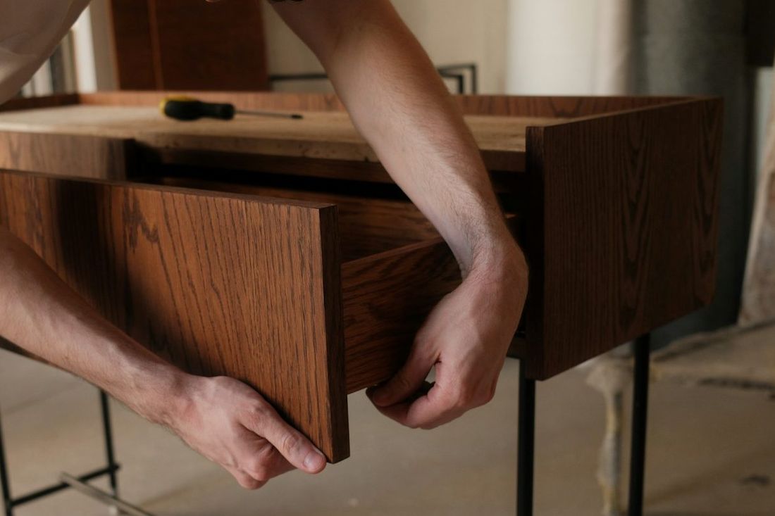 Hände richten die Schublade einer massiven Holzkommode bei der Möbelmontage aus.