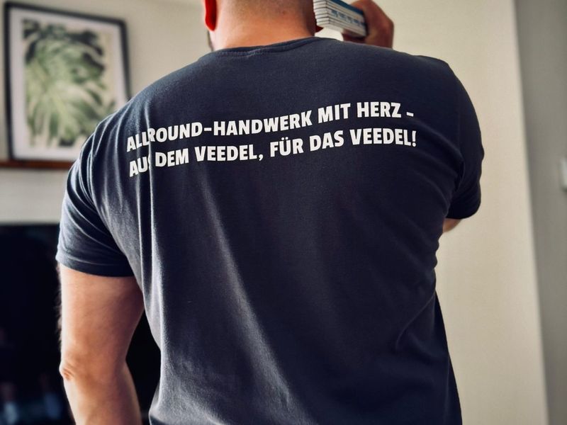 Rückseite des Arbeitsshirts mit dem Aufdruck „Allround-Handwerk mit Herz – aus dem Veedel, für das Veedel!“.